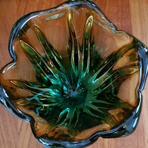 May include: A green and amber glass bowl with a flower-like design. The bowl has a deep center and a wide, flared rim.