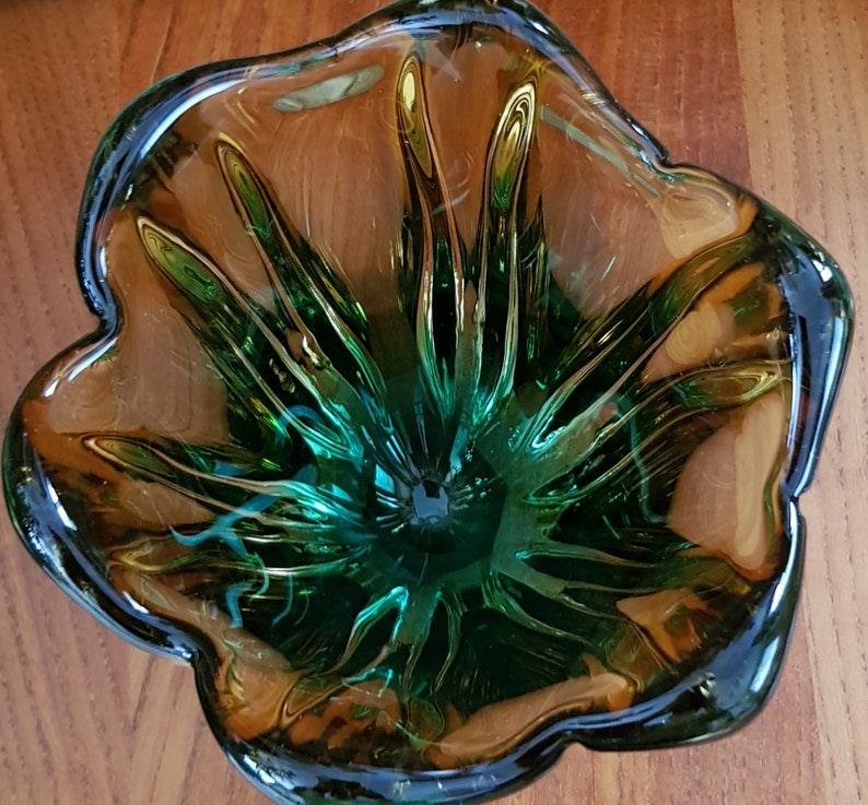 May include: A green and amber glass bowl with a flower-like design. The bowl has a deep center and a wide, flared rim.