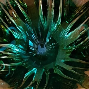 May include: A close-up of a green glass bowl with a unique, textured design. The bowl has a deep, circular shape and a smooth, reflective surface.