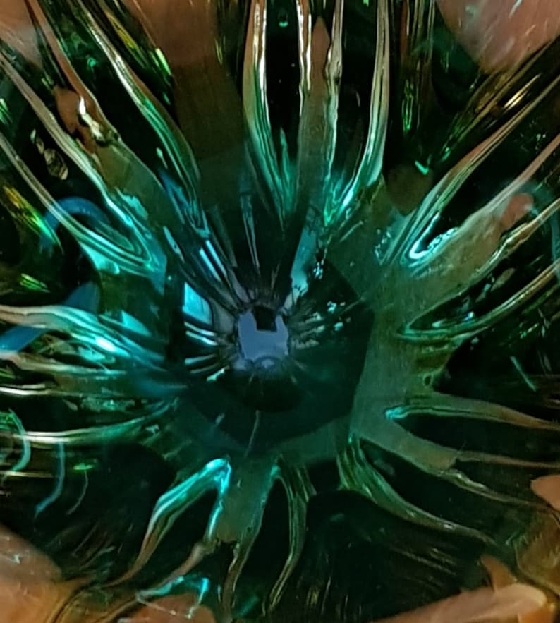 May include: A close-up of a green glass bowl with a unique, textured design. The bowl has a deep, circular shape and a smooth, reflective surface.
