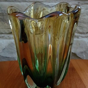 May include: A green and amber glass vase with a wavy, organic shape. The vase has a textured, rippled surface.