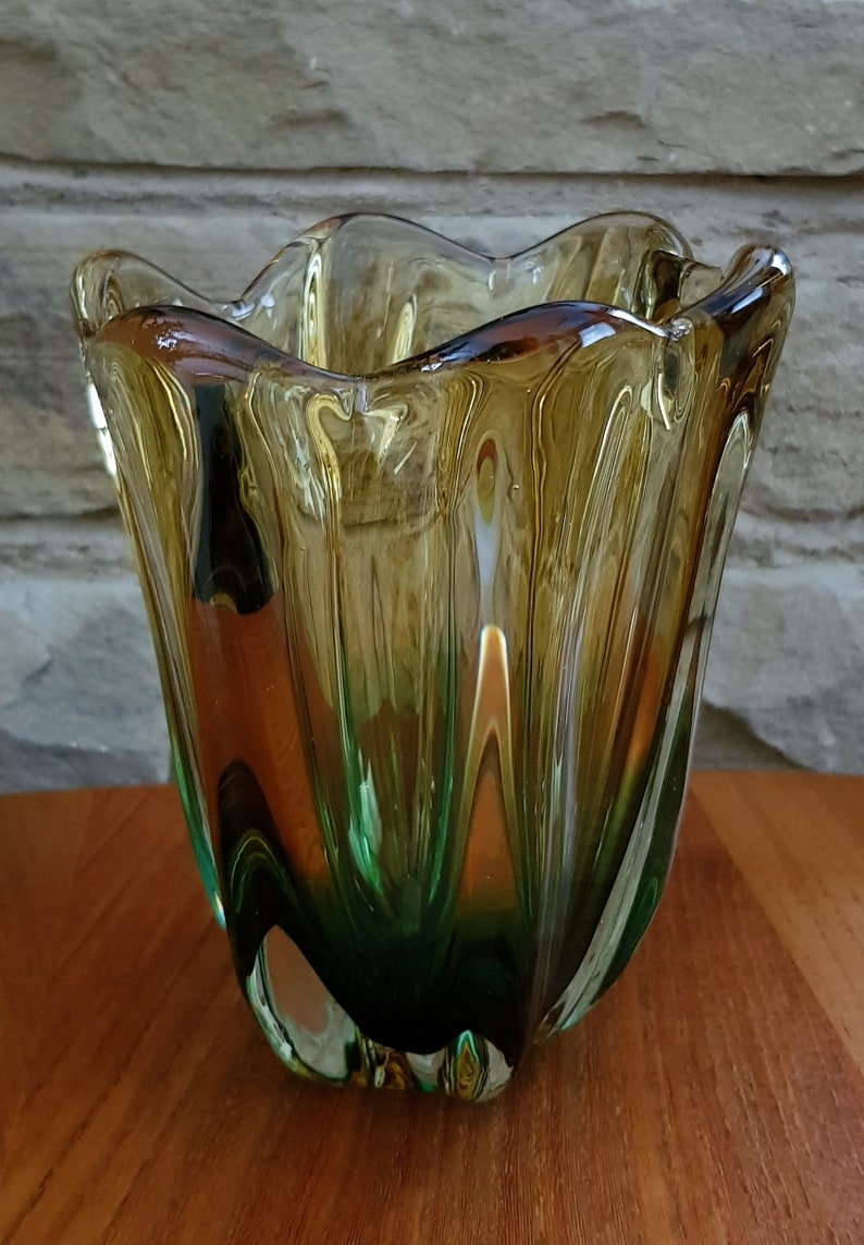 May include: A green and amber glass vase with a wavy, organic shape. The vase has a textured, rippled surface.