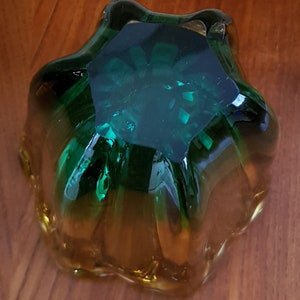 May include: A green and amber glass bowl with a starburst design. The bowl is made of thick glass and has a smooth, polished finish.