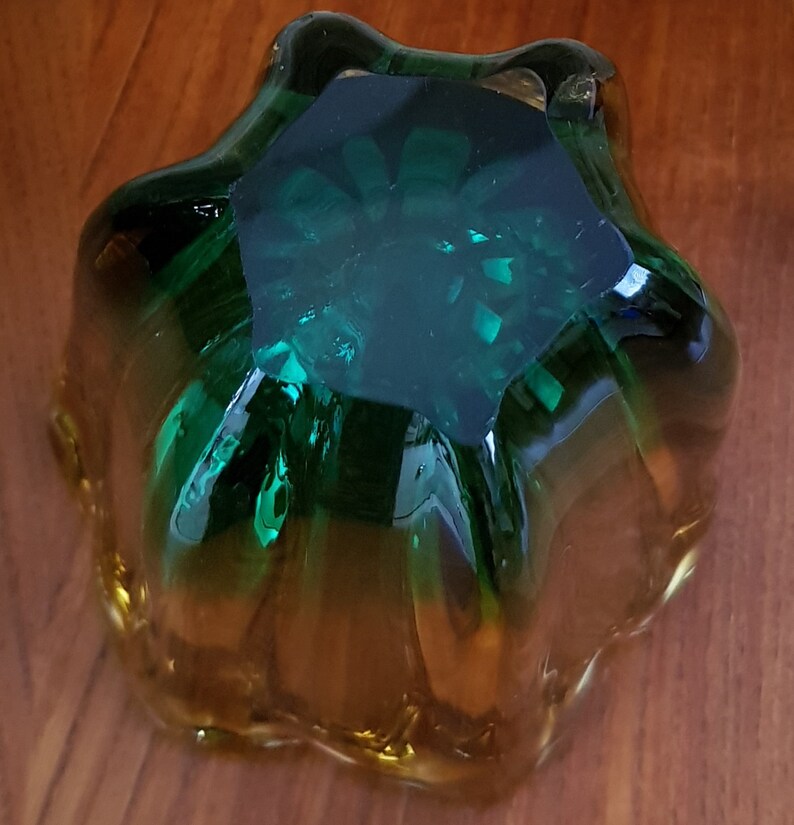 May include: A green and amber glass bowl with a starburst design. The bowl is made of thick glass and has a smooth, polished finish.
