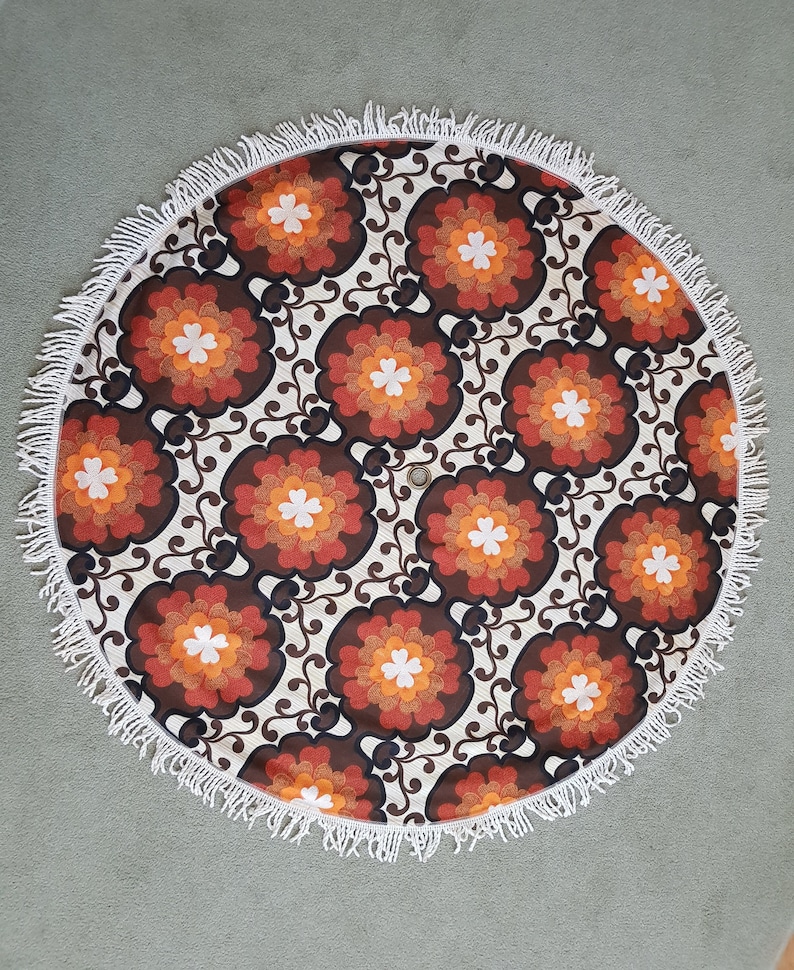 May include: Round white tablecloth with a brown, orange, and white floral pattern and a white fringe border.