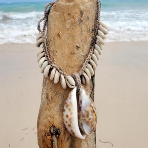 Pode incluir: Um colar de conchas marrom e branco com um grande pingente de concha marrom e branco. O colar é feito de materiais naturais e é perfeito para um visual de praia.