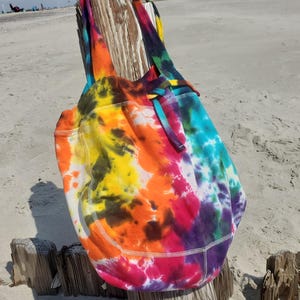 May include: A tie-dye tote bag with a rainbow of colors, including yellow, orange, red, purple, and blue. The bag has a drawstring closure and is made of a soft, comfortable fabric.