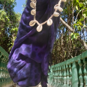 May include: A purple tie-dye sarong with a shell necklace made of cowrie shells. The sarong is worn by a person walking on a path with a green railing.
