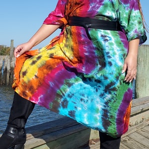 May include: A long, colorful tie-dye dress with a black belt. The dress has a loose, flowing fit and is made of a soft, comfortable fabric. The model is wearing black boots.