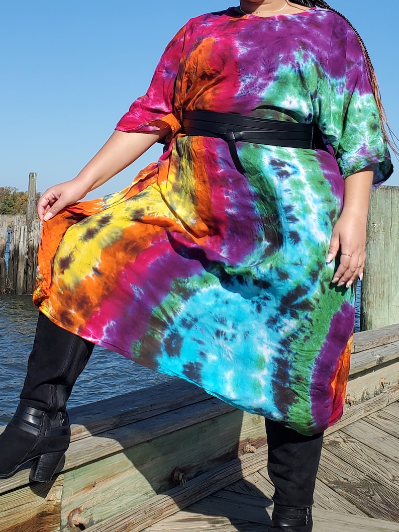 May include: A long, colorful tie-dye dress with a black belt. The dress has a loose, flowing fit and is made of a soft, comfortable fabric. The model is wearing black boots.
