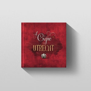 May include: A red book cover with the title "Il Cigno di Utrecht" in gold lettering. A small soccer ball is in the center of the cover.