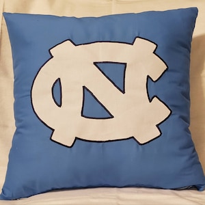 May include: A blue pillow with a white embroidered North Carolina Tar Heels logo.