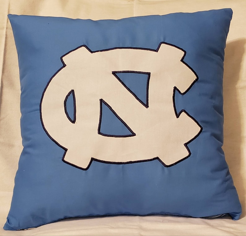 May include: A blue pillow with a white embroidered North Carolina Tar Heels logo.