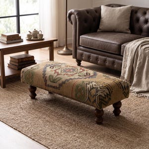 Peut inclure: Un pouf rectangulaire doté d'un tissu tissé texturé avec un motif géométrique multicolore dans des tons de beige, vert, bleu et rouge. Le meuble est soutenu par quatre pieds en bois tourné brun foncé au design arrondi et bombé.