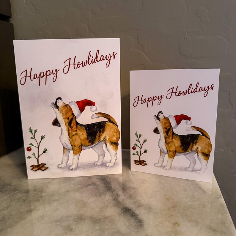 May include: Two white greeting cards with the text "Happy Howlidays" in burgundy script. Each card features a watercolor illustration of a beagle wearing a Santa hat and howling. A small Christmas tree is also depicted.