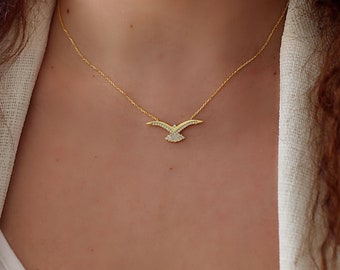May include: A gold-toned necklace featuring a delicate bird-shaped pendant. The wings and tail of the bird are embellished with small, clear, sparkling stones. The pendant is suspended from a thin, matching gold-toned chain that rests on the neck.