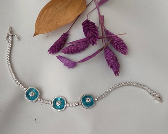Puede incluir: Una pulsera de plata con tres dijes de ojo turco azul turquesa. La pulsera está hecha de pequeñas cuentas de plata y tiene un diseño delicado.