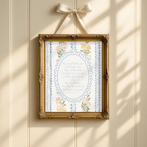 Puede incluir: Una impresión enmarcada con un marco dorado ornamentado, con un diseño floral y texto. La impresión está suspendida por una cinta color crema atada en un lazo. El texto dice: "The Lord bless you and keep you..."