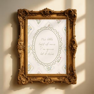 Puede incluir: Marco de fotos dorado ornamentado con un fondo floral. El marco rodea un diseño ovalado con el texto "This little light of mine I'm gonna let it shine" en una fuente manuscrita.