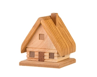 Könnte beinhalten: Ein kleines Holzmodell eines Hauses mit einem braunen Dach und einem Schornstein. Das Haus hat zwei Fenster und eine Tür.