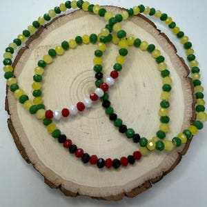 May include: Three necklaces with faceted beads in yellow, green, red, white, and black. The necklaces are displayed on a round wooden surface with a natural wood grain.