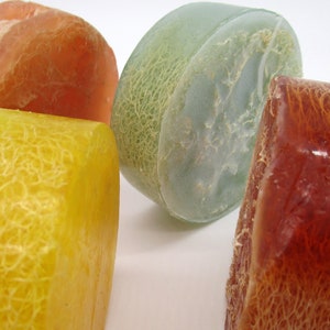 May include: Four loofah bath sponges in different colors: orange, yellow, green, and brown. The sponges are round and have a textured surface.