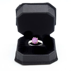 Puede incluir: Un anillo de plata con una piedra preciosa rosa en una caja de anillo negra.