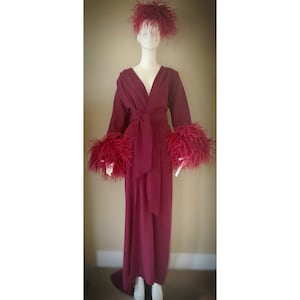 May include: A long, burgundy robe with a V-neckline and a sash tie. The robe has feather trim on the cuffs and a feather headband.