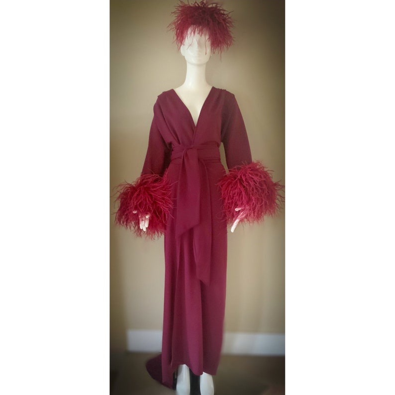 May include: A long, burgundy robe with a V-neckline and a sash tie. The robe has feather trim on the cuffs and a feather headband.
