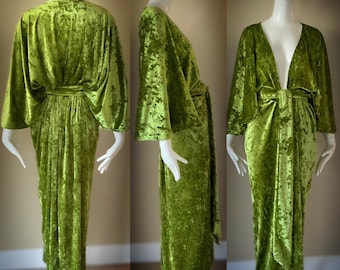 Op de afbeelding: Een lange groene fluwelen robe met een diepe V-hals en wijde mouwen. De robe is in de taille gebonden met een ceintuur.