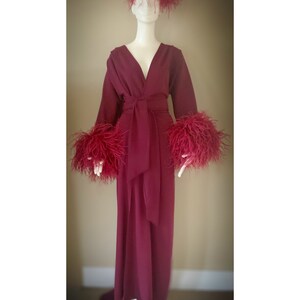 May include: A long, burgundy robe with a V-neckline and a sash tie. The robe has feather trim on the cuffs and a feather headband.