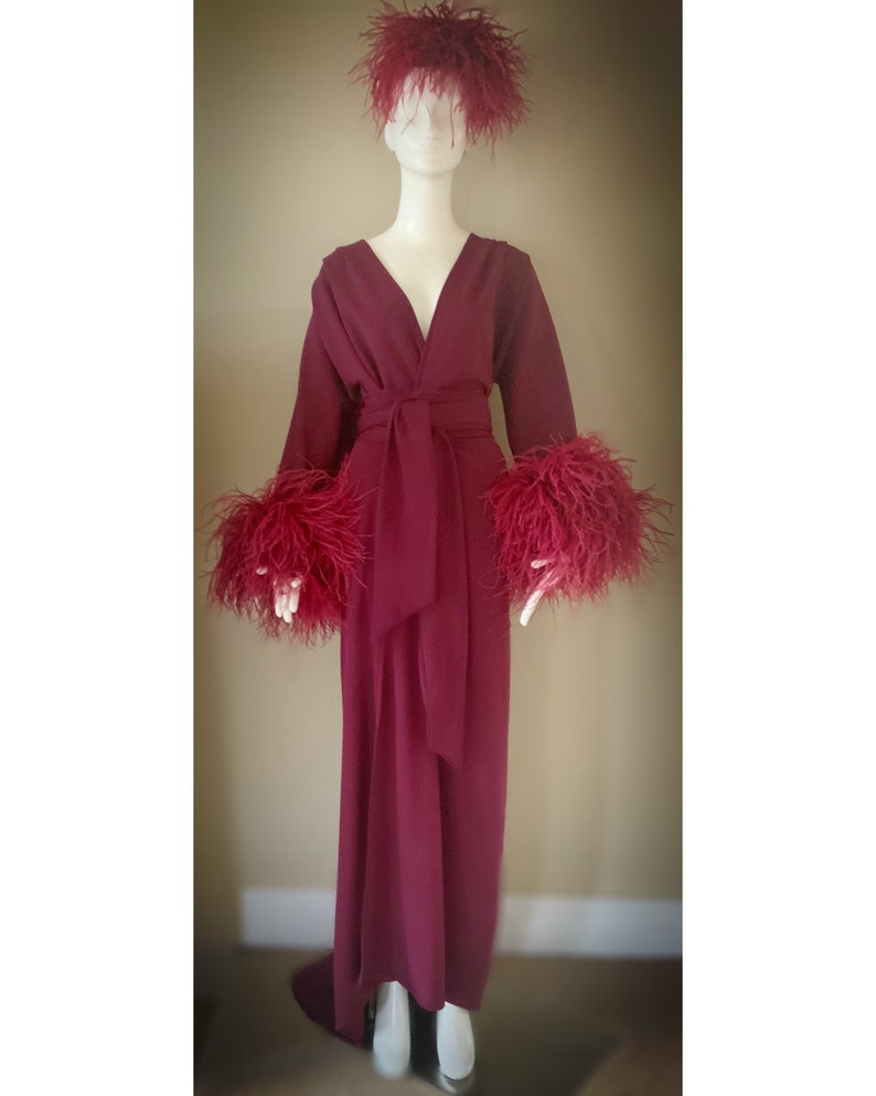 May include: A long, burgundy robe with a V-neckline and a sash tie. The robe has feather trim on the cuffs and a feather headband.