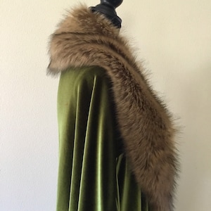 Puede incluir: Una capa de terciopelo verde con un cuello de piel sint&eacute;tica marr&oacute;n. El cuello es grueso y esponjoso, y envuelve el cuello.