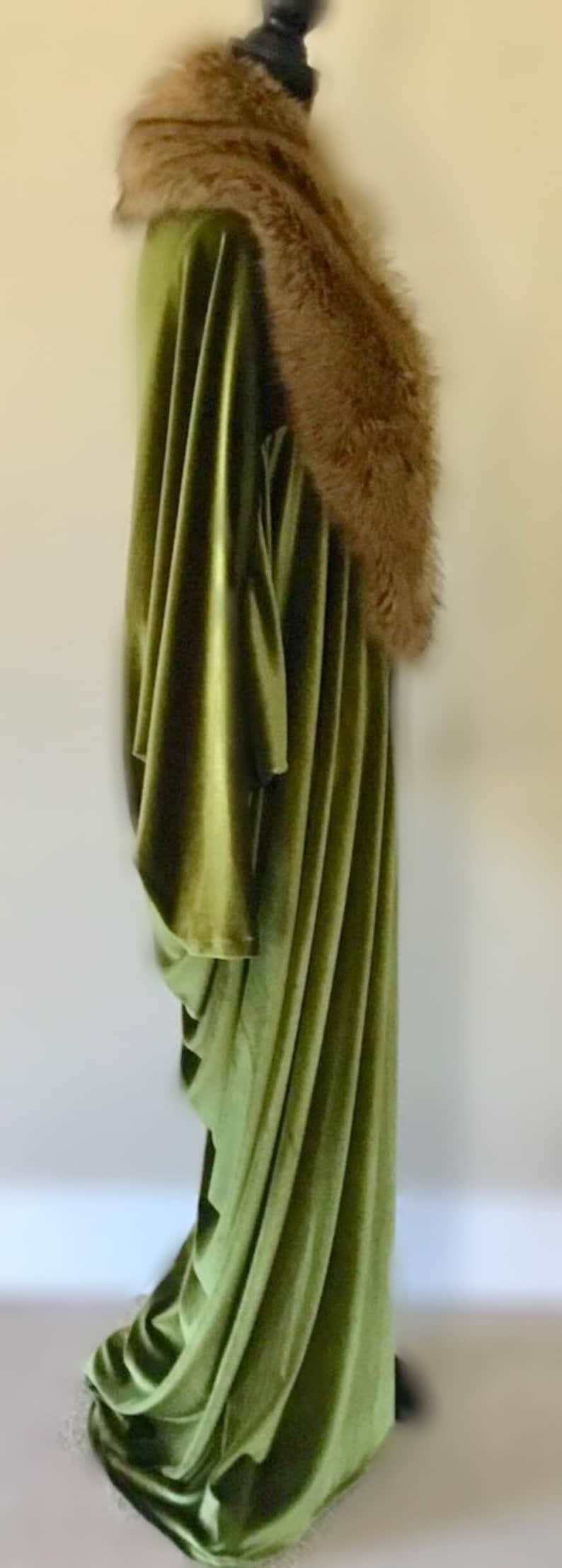 Puede incluir: Una larga t&uacute;nica de terciopelo verde con un cuello de piel marr&oacute;n. La t&uacute;nica est&aacute; drapeada sobre un maniqu&iacute; y tiene un dise&ntilde;o fluido y elegante.