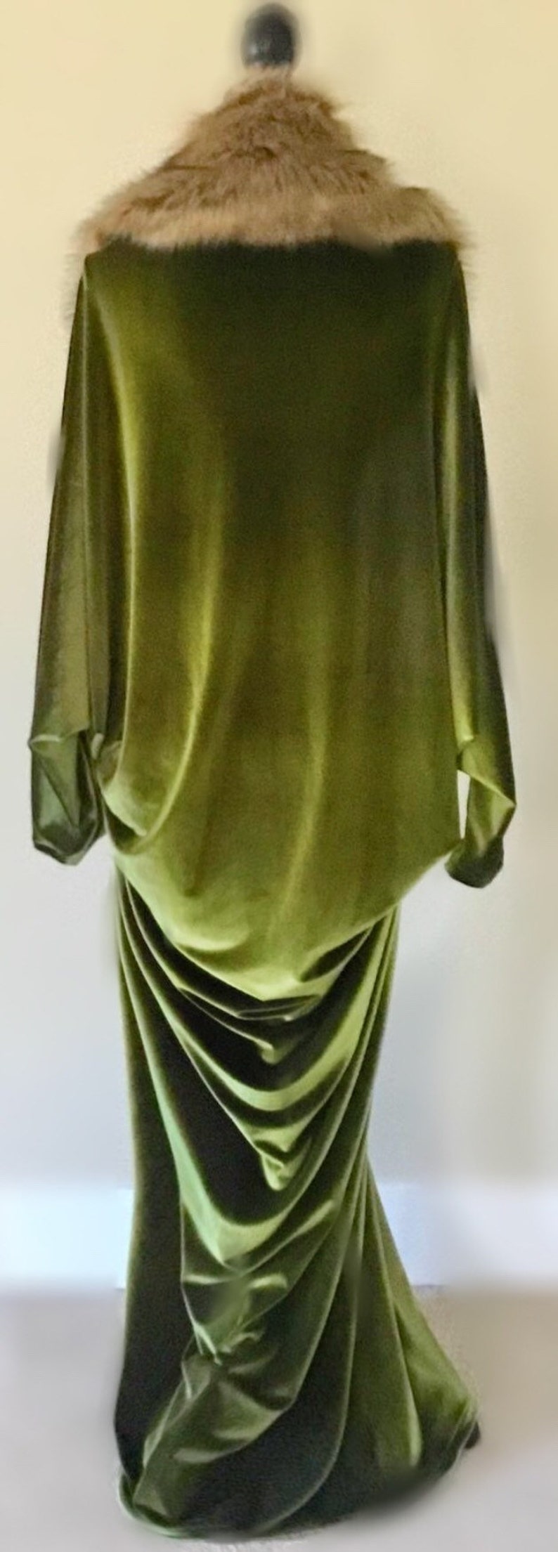 Puede incluir: Un vestido largo de terciopelo verde con un cuello de piel sint&eacute;tica marr&oacute;n. El vestido tiene un dise&ntilde;o fluido y drapeado, perfecto para una ocasi&oacute;n especial.