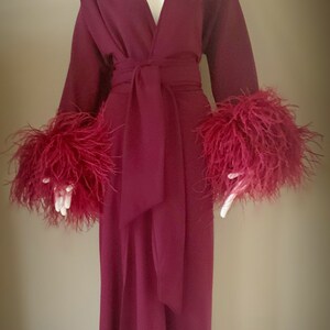 May include: A long, burgundy robe with a V-neckline and a sash tie. The robe has feather trim on the cuffs and a feather headpiece.