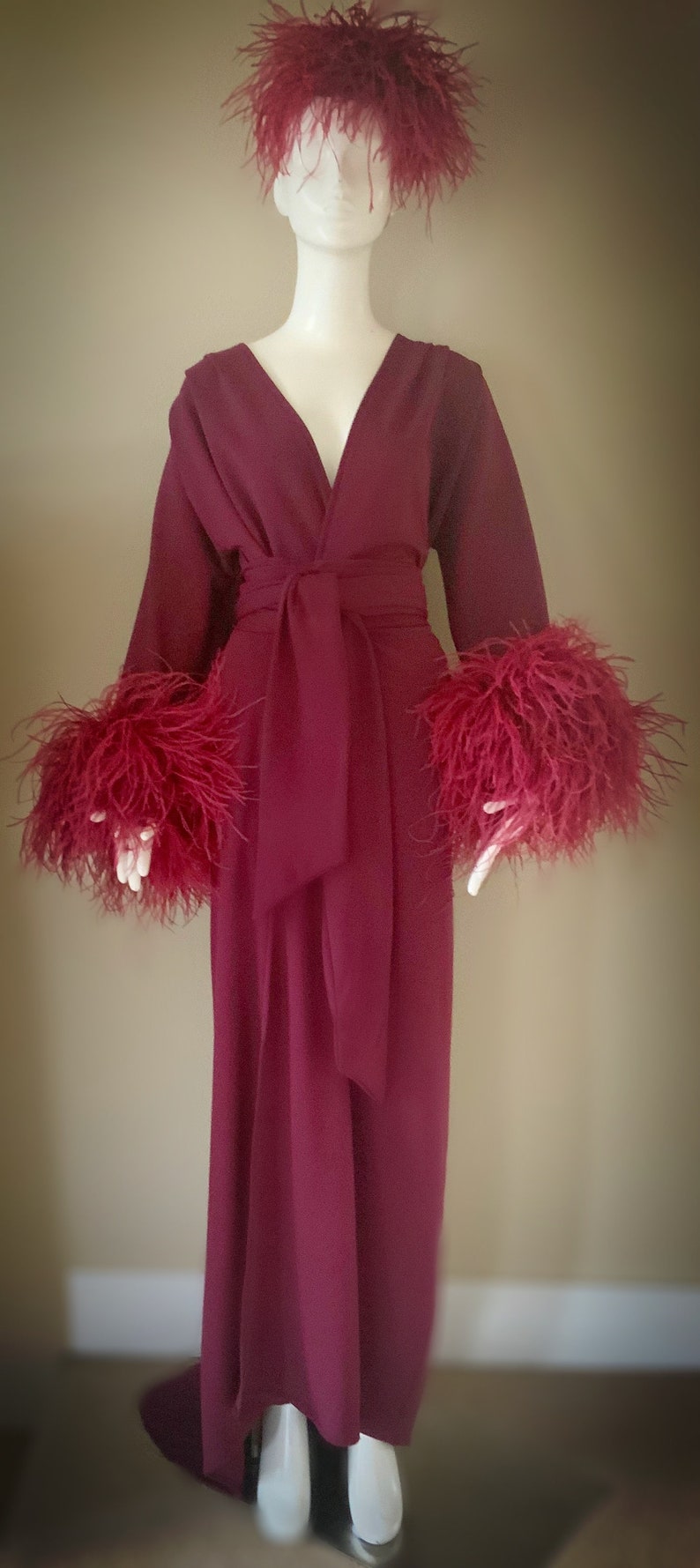 May include: A long, burgundy robe with a V-neckline and a sash tie. The robe has feather trim on the cuffs and a feather headpiece.