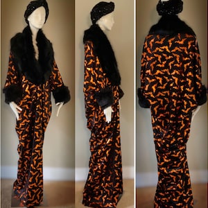 May include: A long, flowing robe with a bat pattern in orange and black, paired with a black fur collar and cuffs. The ensemble includes a matching black headband. The robe is displayed on a mannequin.