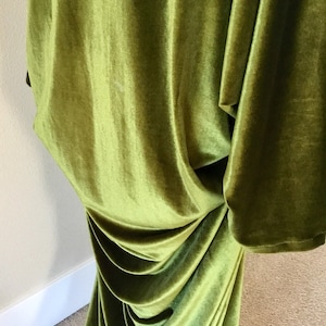 Puede incluir: Un vestido largo de terciopelo verde fluido con un dise&ntilde;o drapeado. El vestido est&aacute; hecho de una tela suave y lujosa y tiene una silueta fluida y elegante.