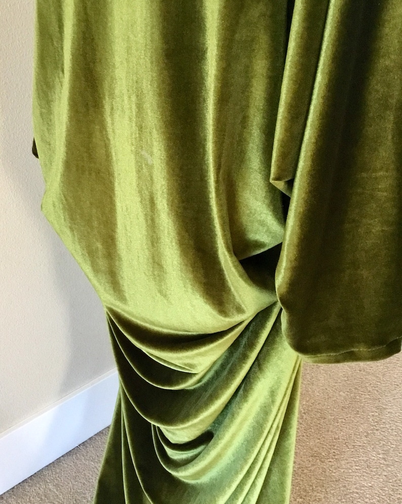 Puede incluir: Un vestido largo de terciopelo verde fluido con un dise&ntilde;o drapeado. El vestido est&aacute; hecho de una tela suave y lujosa y tiene una silueta fluida y elegante.