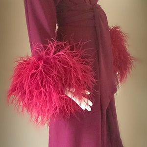 May include: A long, burgundy robe with a deep V-neckline and feather trim on the cuffs and collar. The robe is made of a soft, flowing fabric and has a tie belt.