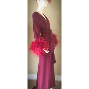 May include: A long, burgundy robe with a deep V-neckline and a sash tie. The robe has feather trim on the cuffs and a feather headpiece.