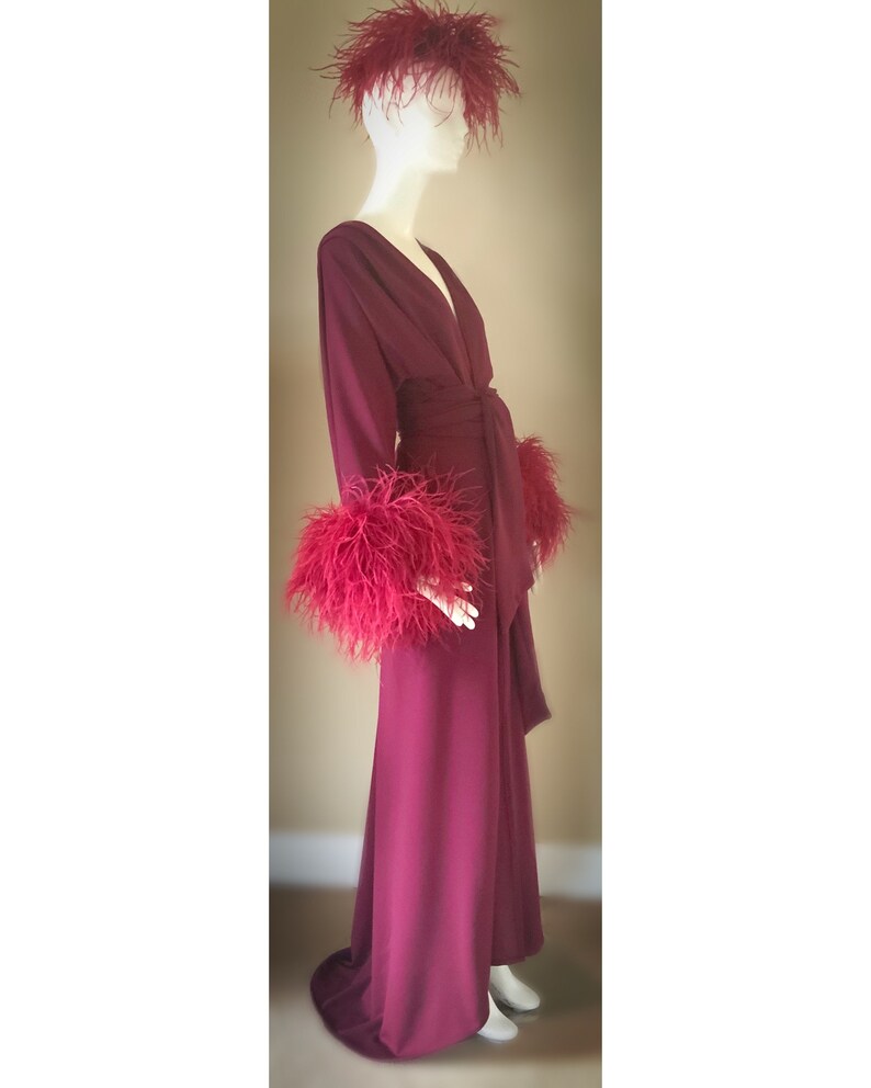May include: A long, burgundy robe with a deep V-neckline and a sash tie. The robe has feather trim on the cuffs and a feather headpiece.