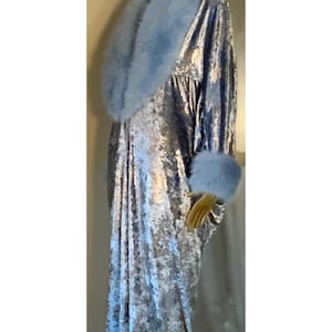 May include: A long, silver-grey velvet robe with a light blue faux fur collar and cuffs. The robe is displayed on a mannequin with a gold head. The fabric has a textured, shimmering appearance.