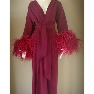 May include: A long, burgundy robe with a V-neckline and a sash tie. The robe has feather trim on the cuffs and a feather headpiece.