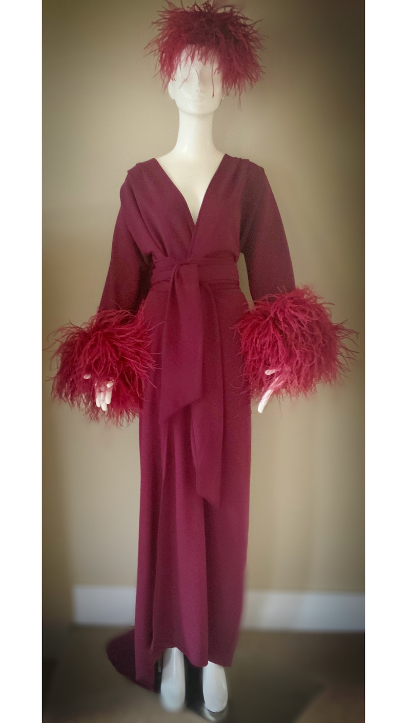 May include: A long, burgundy robe with a V-neckline and a sash tie. The robe has feather trim on the cuffs and a feather headpiece.