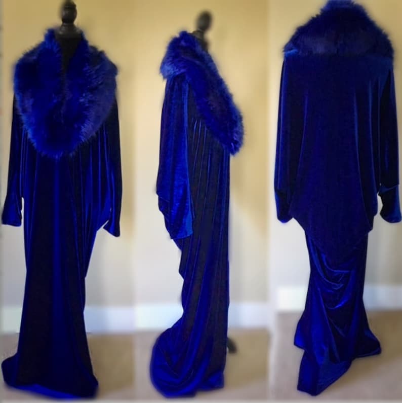 May include: A royal blue velvet gown with a faux fur collar. The long-sleeved dress has a flowing silhouette and is displayed on a mannequin. The faux fur collar is a deep blue color, complementing the velvet fabric.