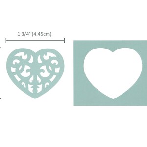 May include: A light blue heart-shaped stencil with a decorative filigree design. The stencil measures 4.45 cm wide and 3.97 cm tall.