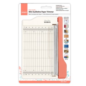 May include: A white and orange mini guillotine paper trimmer with a metal blade. The trimmer has a ruler with markings in inches and centimeters. The packaging includes instructions for use and a list of materials that can be cut with the trimmer.