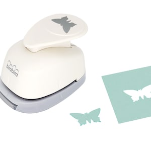 May include: A white paper punch with a gray butterfly design on the top. The punch is used to create butterfly shapes from paper. A green butterfly shape has been punched out of a piece of green paper.